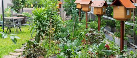 Un jardín con casas de pájaros de madera, diversas plantas y una zona de estar con mesas y sillas.