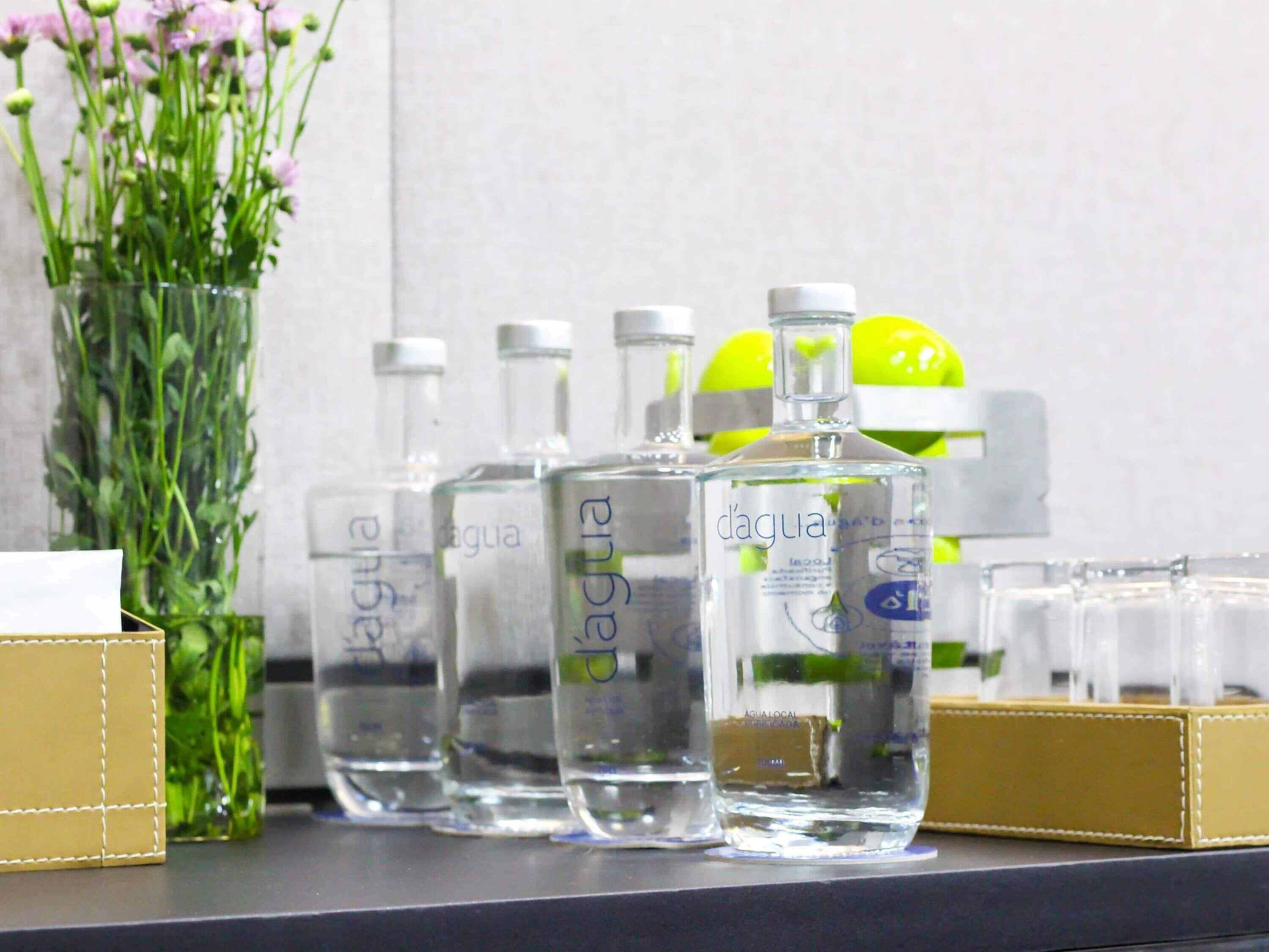 A row of clear bottles with labels, a vase with flowers, and a yellow object on a shelf.
