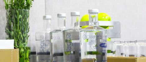 A row of clear bottles with labels, a vase with flowers, and a yellow object on a shelf.