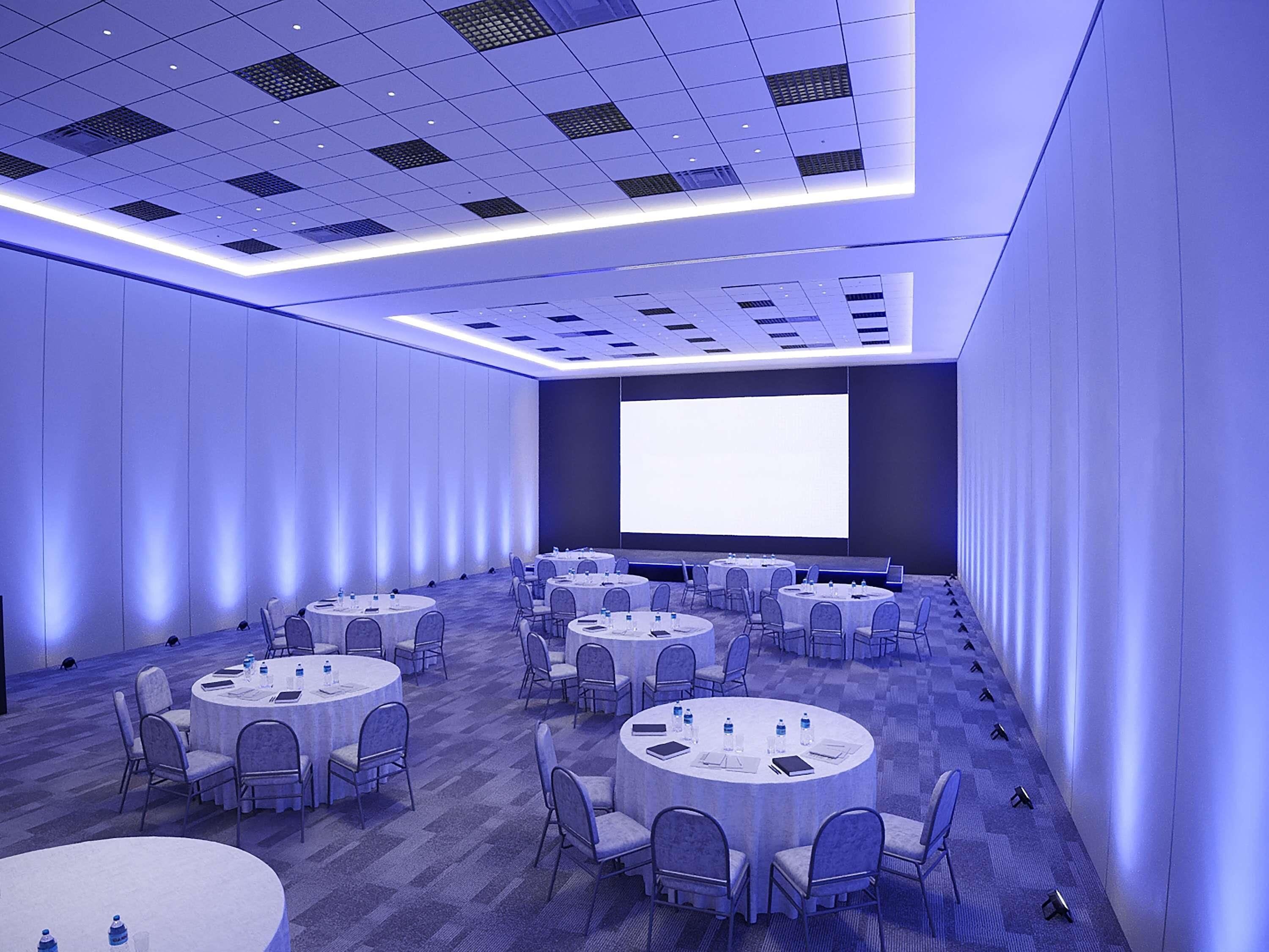 A conference room with multiple round tables and chairs, a large screen, and a carpeted floor.