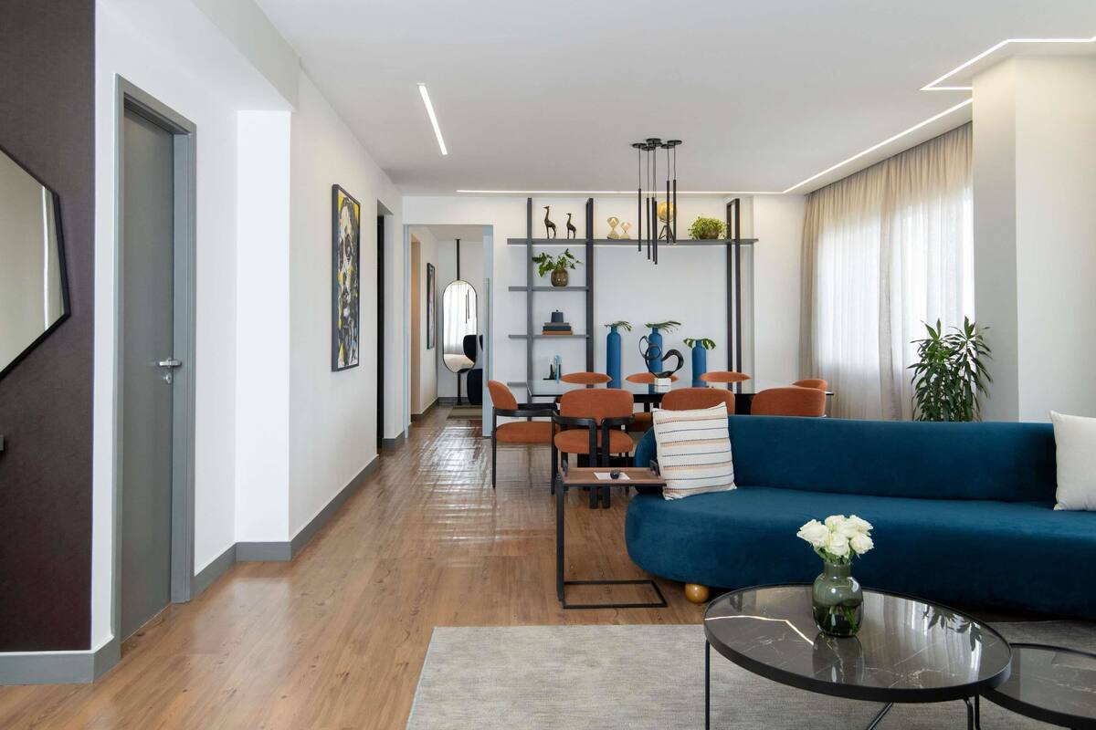 Uma sala de estar moderna com um sofá azul, uma mesa de centro e um espaço de jantar com cadeiras e mesa.