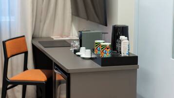 Quarto de hotel moderno com escrivaninha, cadeira, máquina de café, caneca, copo e caixa de lenços.
