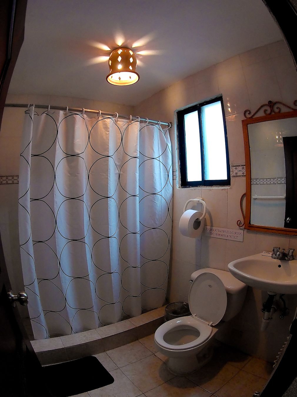 A bathroom with a shower curtain, toilet, sink, and a window.