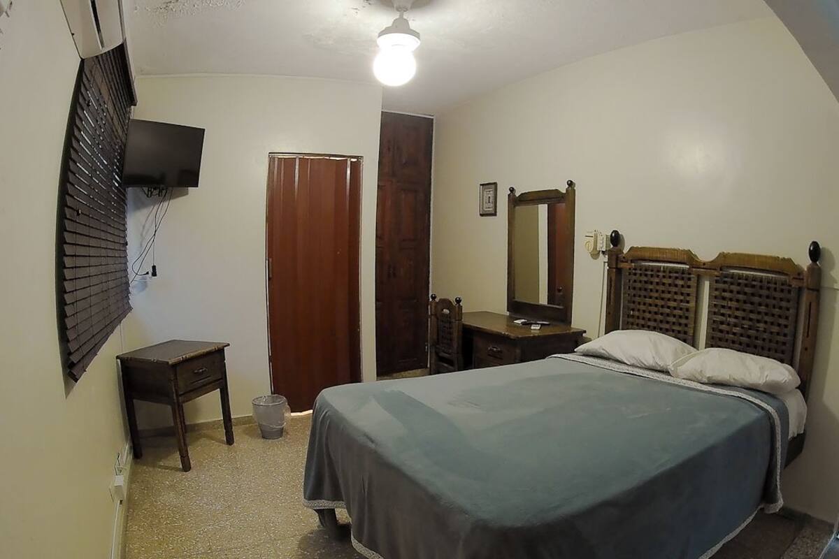 Une chambre à coucher comprenant un lit, un bureau, une chaise, un miroir et un téléviseur fixé au mur.