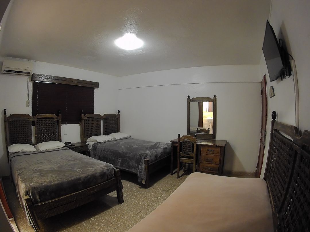 Quarto com duas camas, cômoda, espelho e televisão na parede.