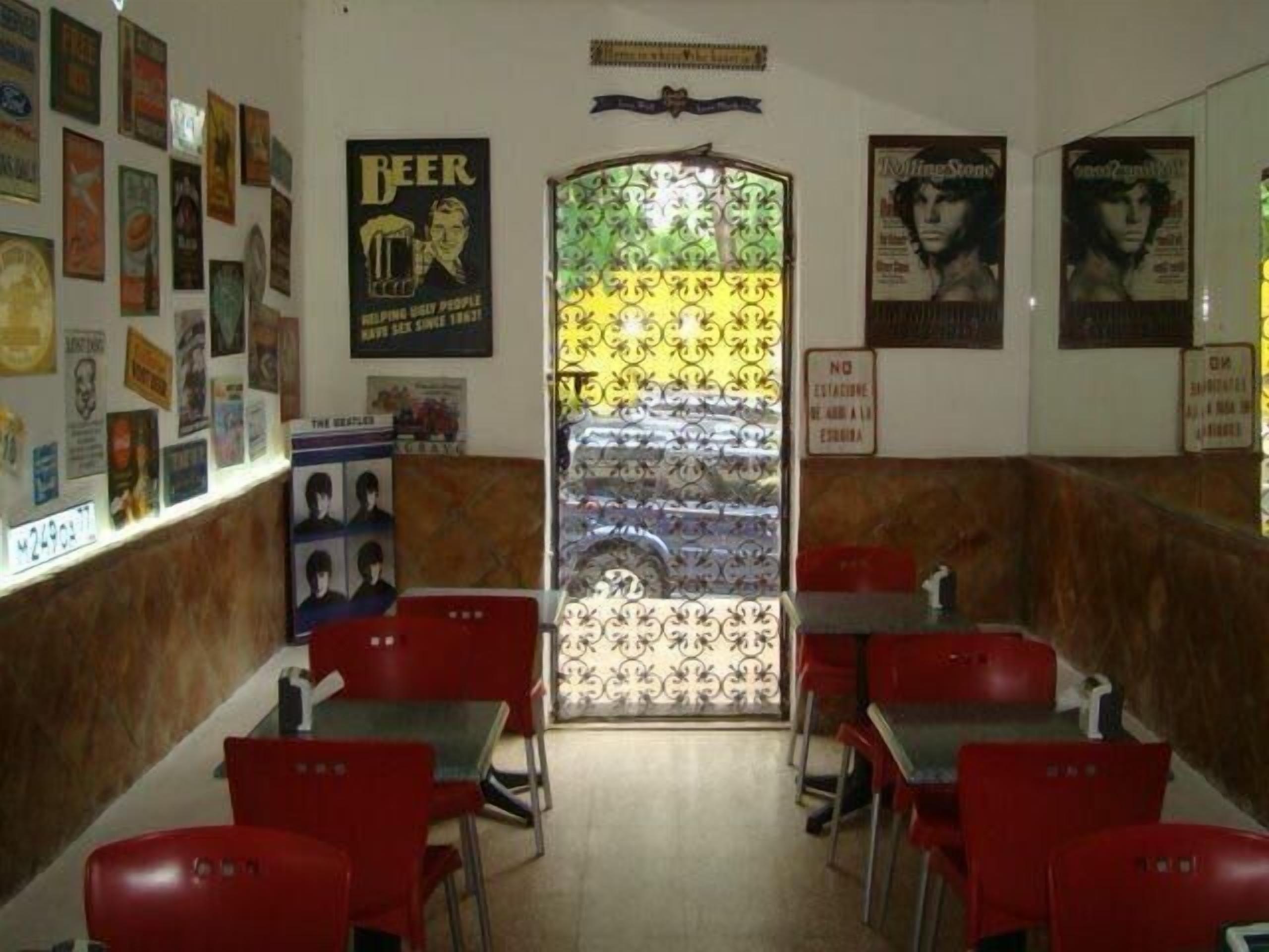 A restaurant interior with red chairs and tables, posters on the walls, and a patterned glass door.
