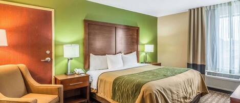 A hotel room with a bed, a chair, a desk, and a lamp.