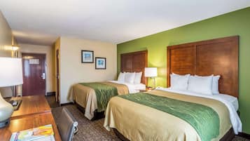 A hotel room with two beds, a desk with a lamp, a chair, and a small table with a magazine.