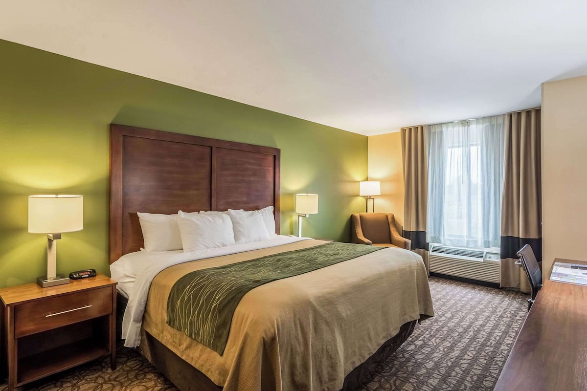 Une chambre d’hôtel avec un grand lit, deux tables de chevet avec des lampes, une chaise, un bureau et une fenêtre avec des rideaux.