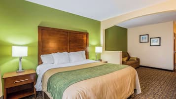 Une chambre d’hôtel avec un grand lit, deux tables de chevet avec des lampes, un mur vert, une moquette marron à motifs et un fauteuil marron.