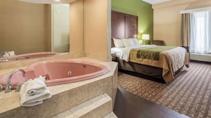 Een hotelkamer met een groot roze bad, een bed met een groen hoofdeinde en een kamerbreed tapijt met een patroon.