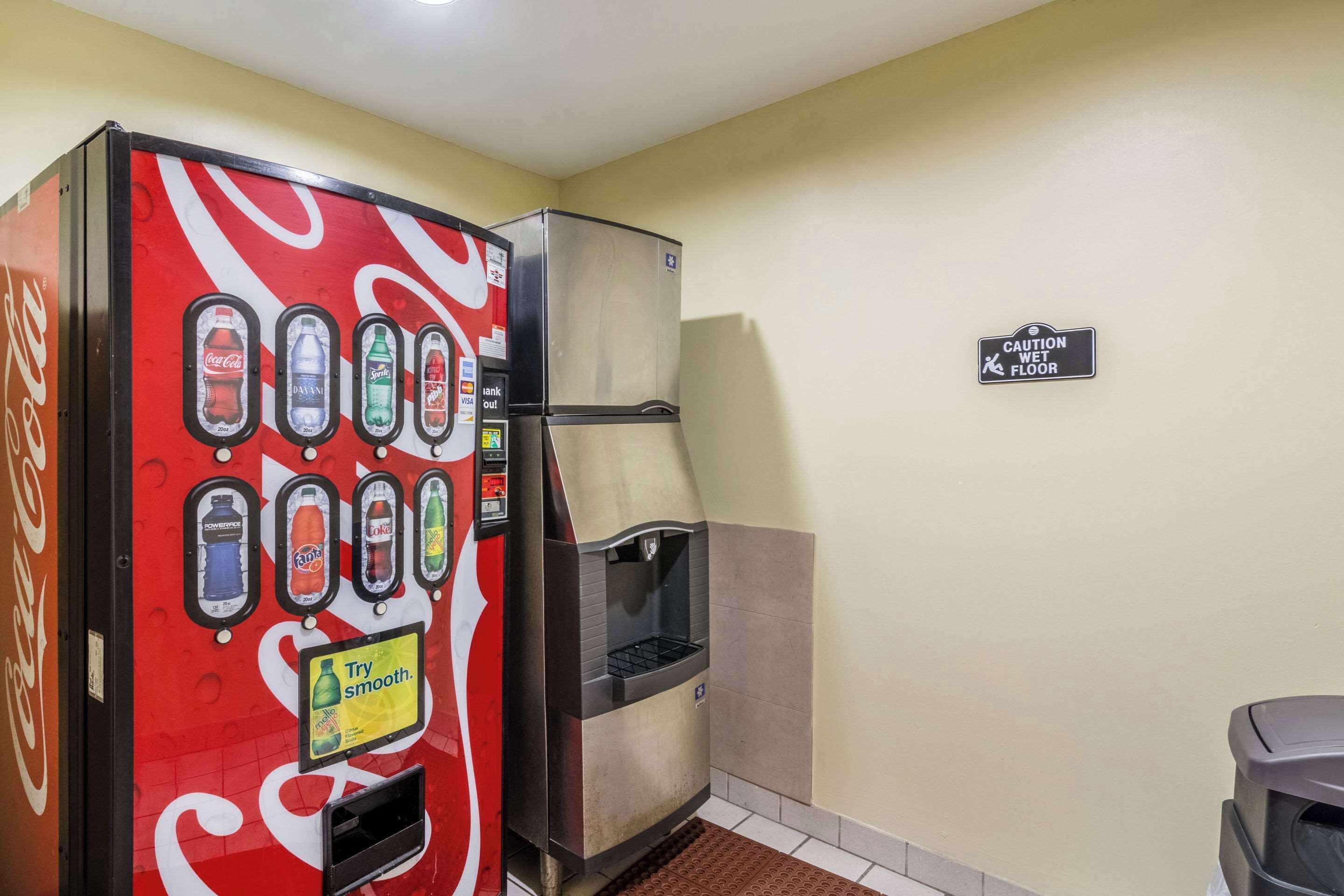 A vending machine with various drink options and a caution wet floor sign on a plain wall.