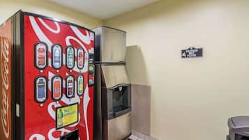 A vending machine with various drink options and a caution wet floor sign on a plain wall.