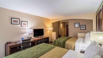 A hotel room with two beds, a desk with a television, a lamp, and framed pictures on the wall.