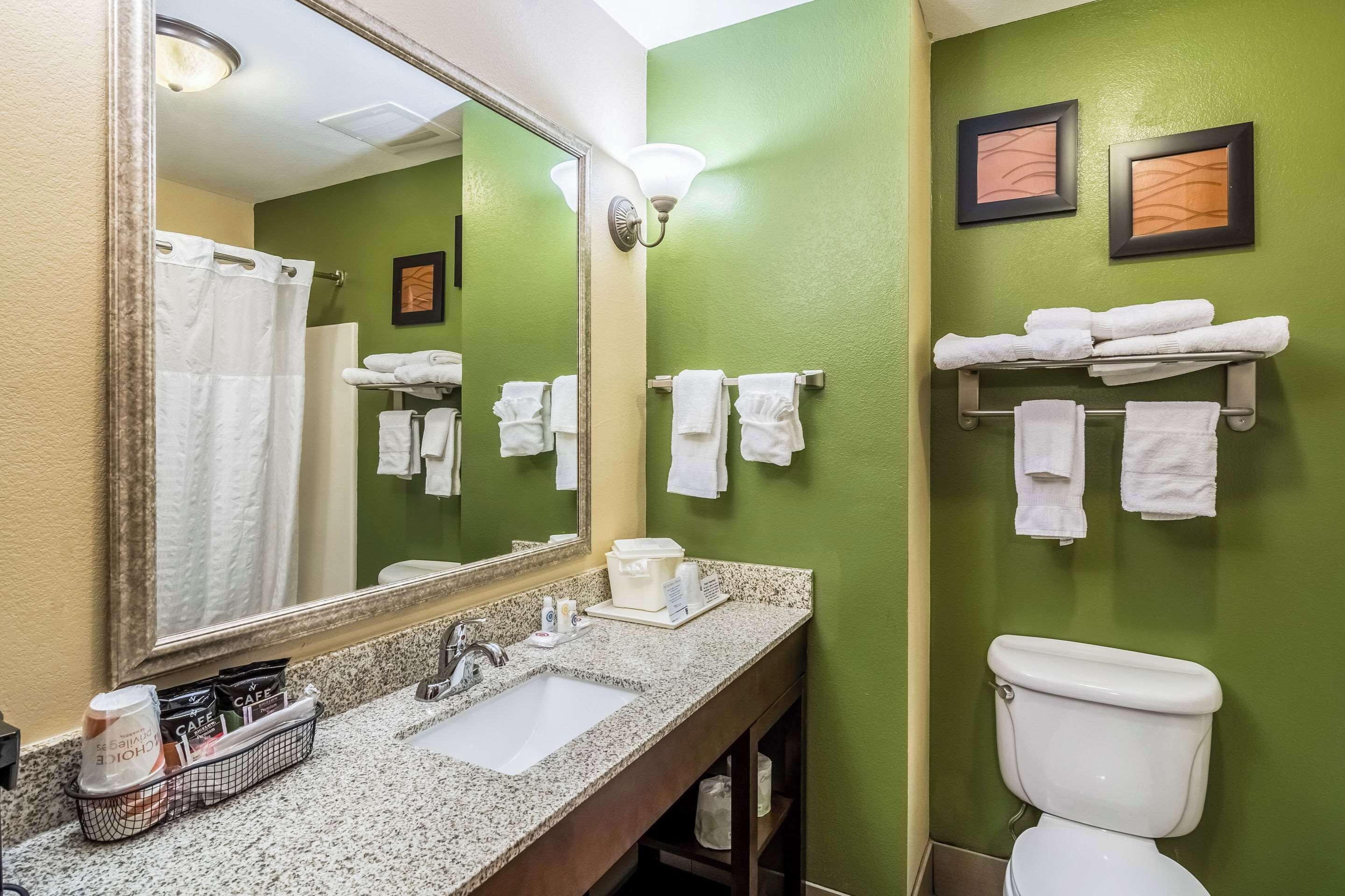 Une salle de bain avec un lavabo, un miroir et des toilettes. Il y a des serviettes sur un porte-serviettes et une étagère.
