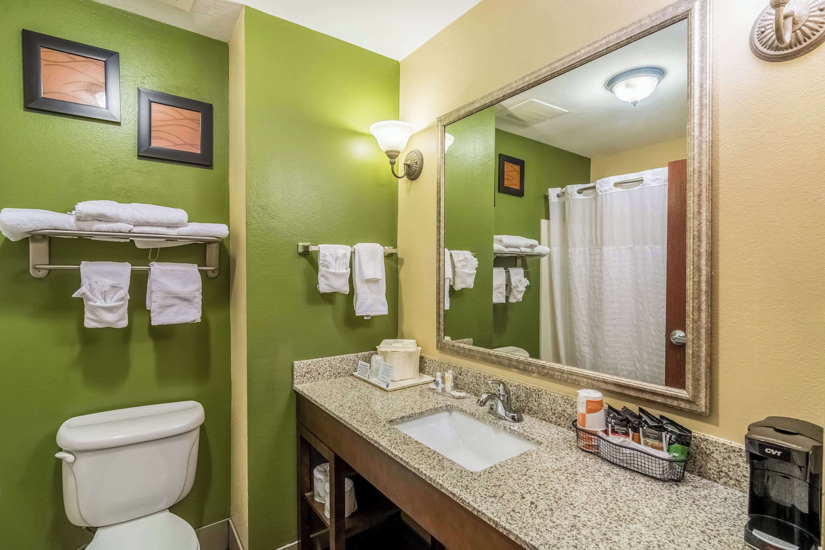 A bathroom with green walls, a white toilet, a sink with toiletries, and a mirror.