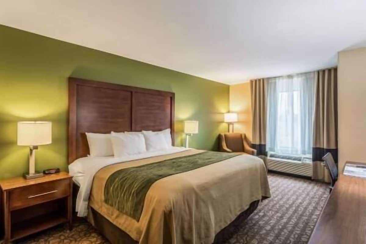 Une chambre d’hôtel comprenant un lit, deux tables de chevet, une chaise, une fenêtre avec des rideaux et un bureau.