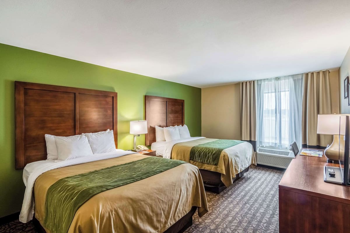 Une chambre d’hôtel avec deux lits, un bureau, une lampe et une fenêtre avec des rideaux.