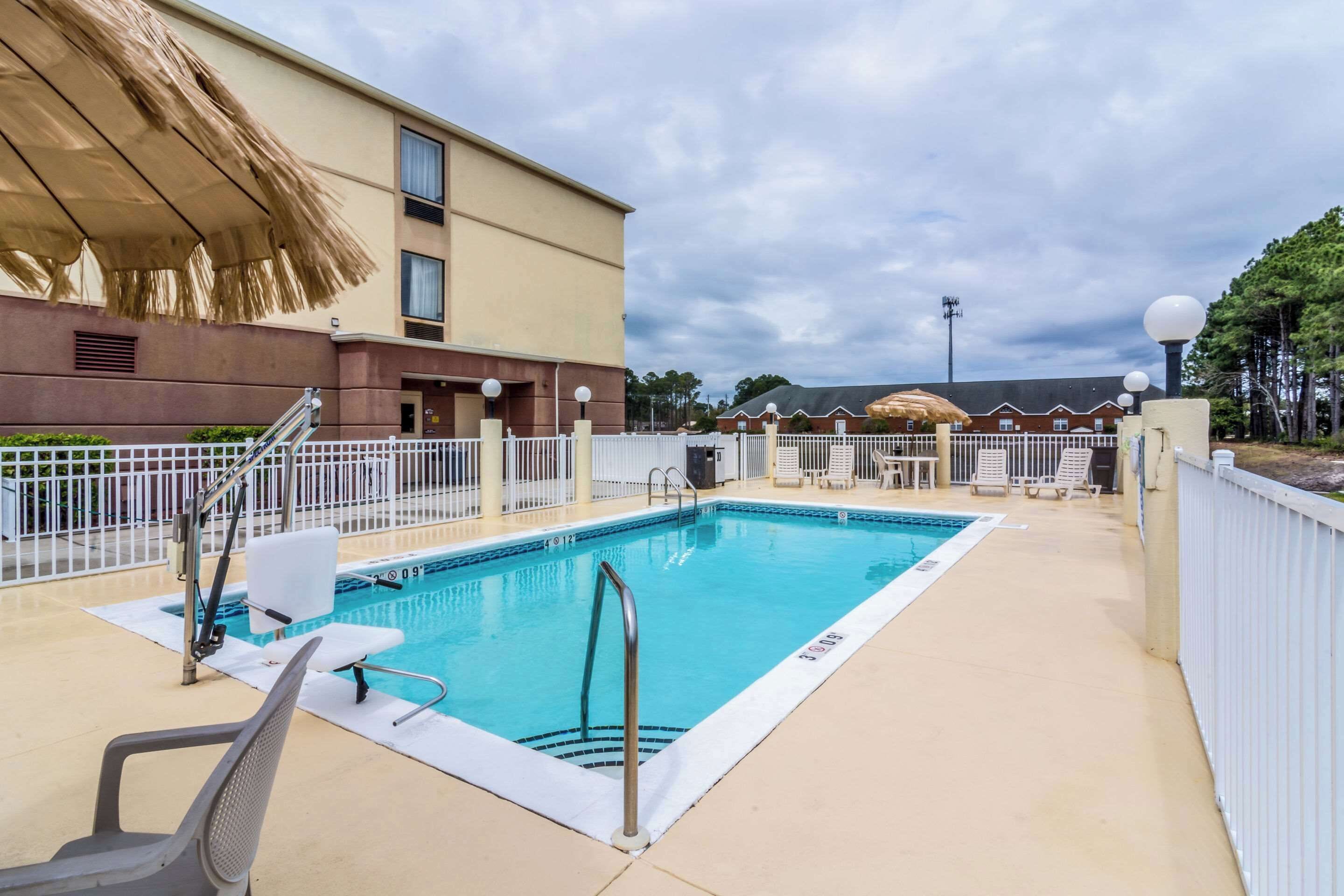 A swimming pool with a white deck, a lifeguard chair, and a fence.