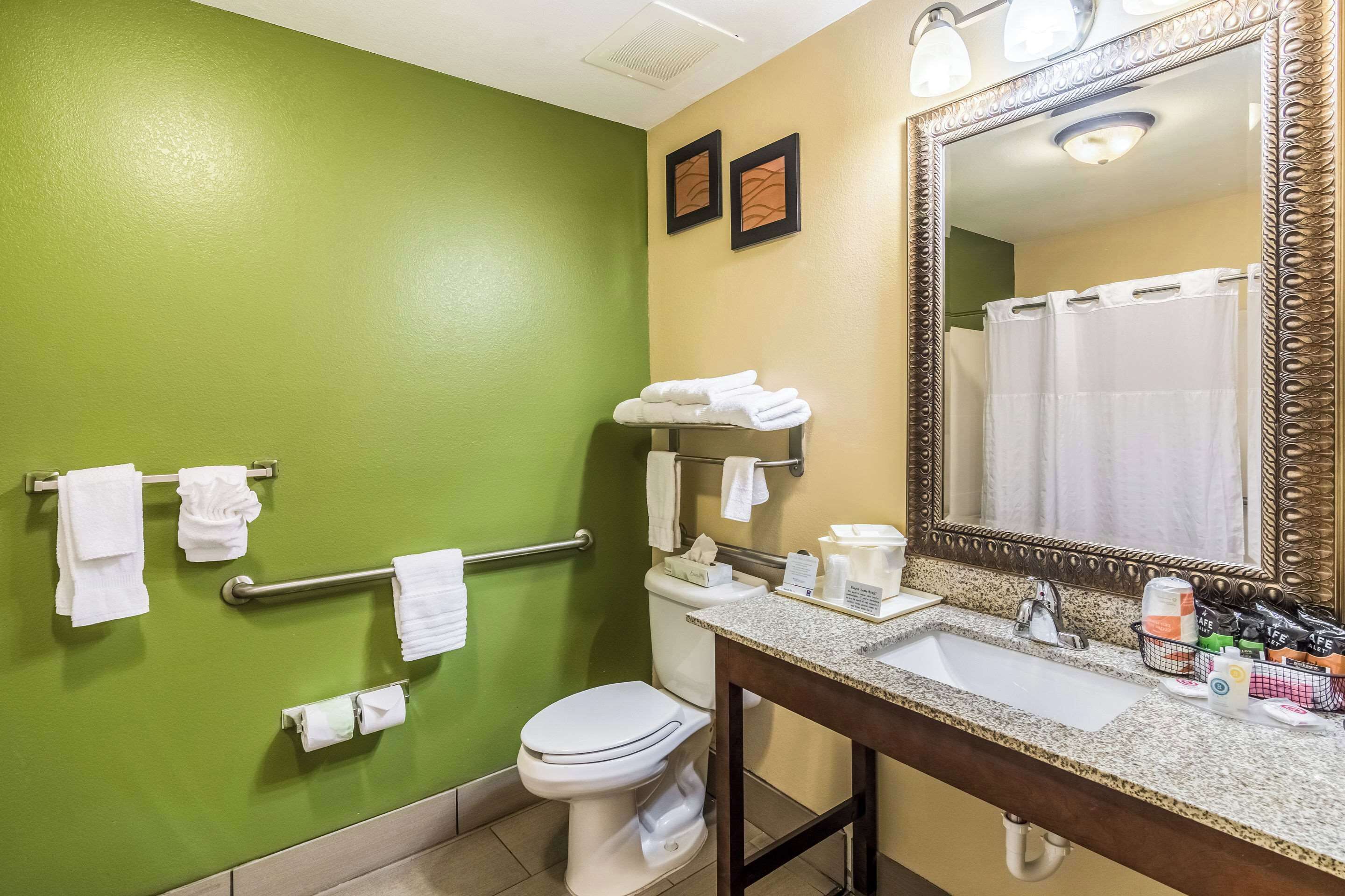 A bathroom with a green wall, a white toilet, a sink with a mirror, and towels on a rack.