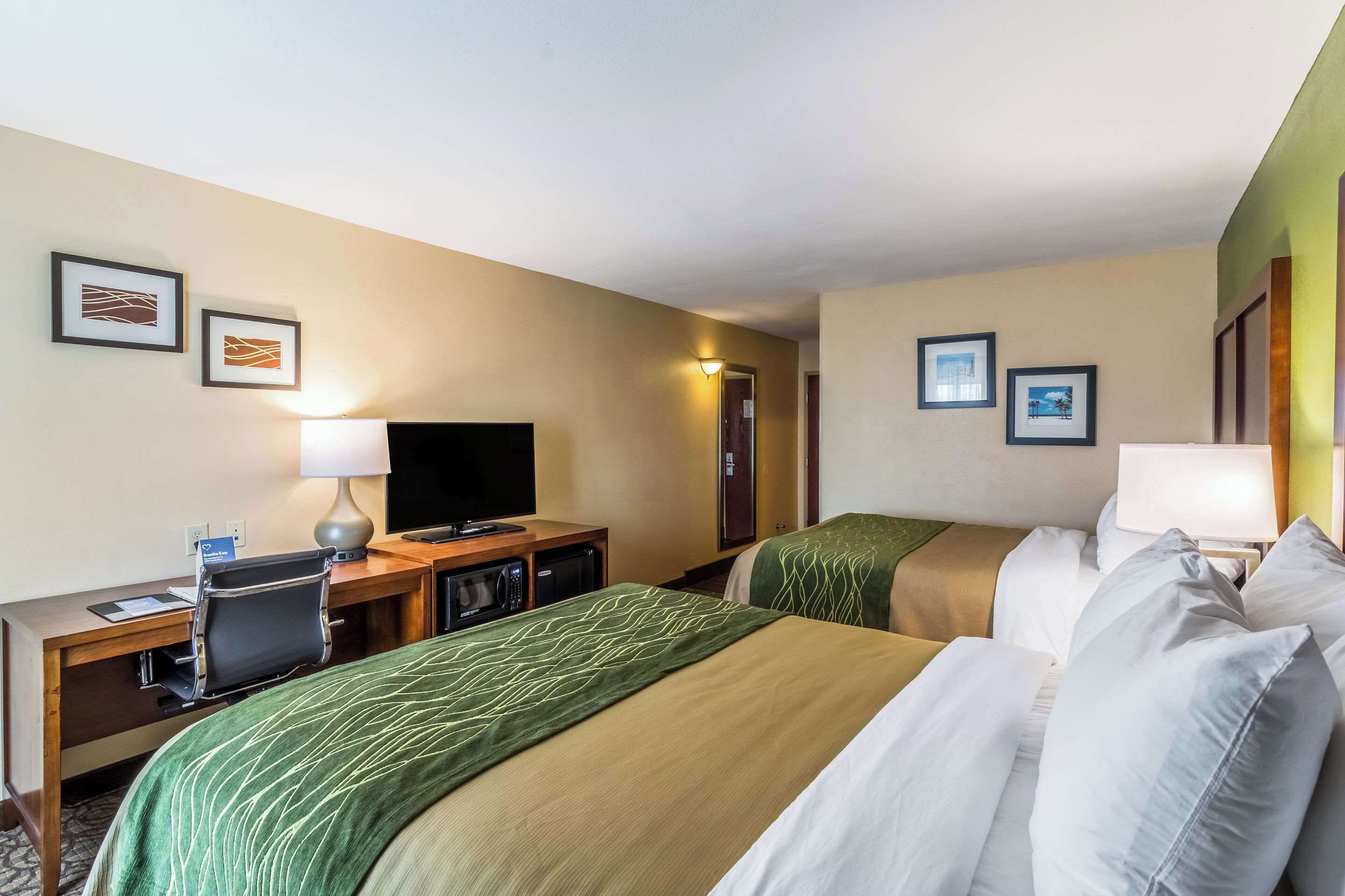 A hotel room with two beds, a desk with a computer, a television, and framed pictures on the wall.