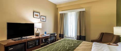 A hotel room with a bed, a TV, a desk with a lamp, a chair, and a window with curtains.