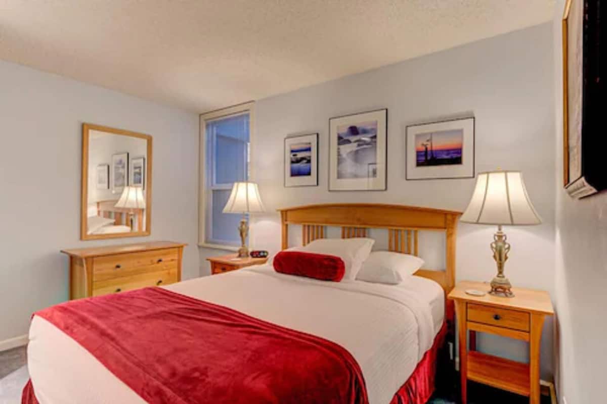 A hotel room with a large bed, two bedside tables, a nightstand, a window, and three framed pictures on the wall.