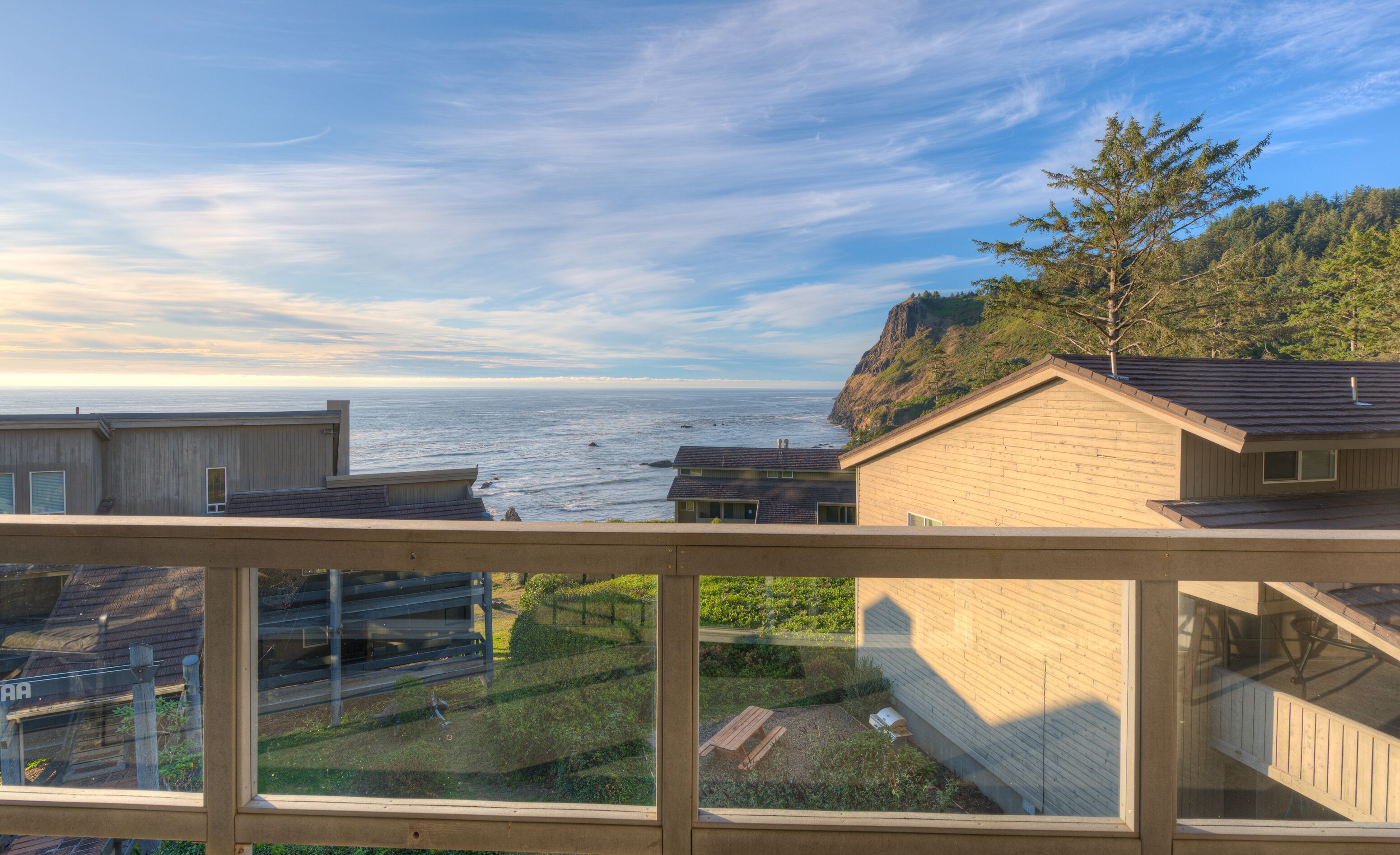 A coastal view from a wooden balcony overlooking the ocean and a forested hillside.