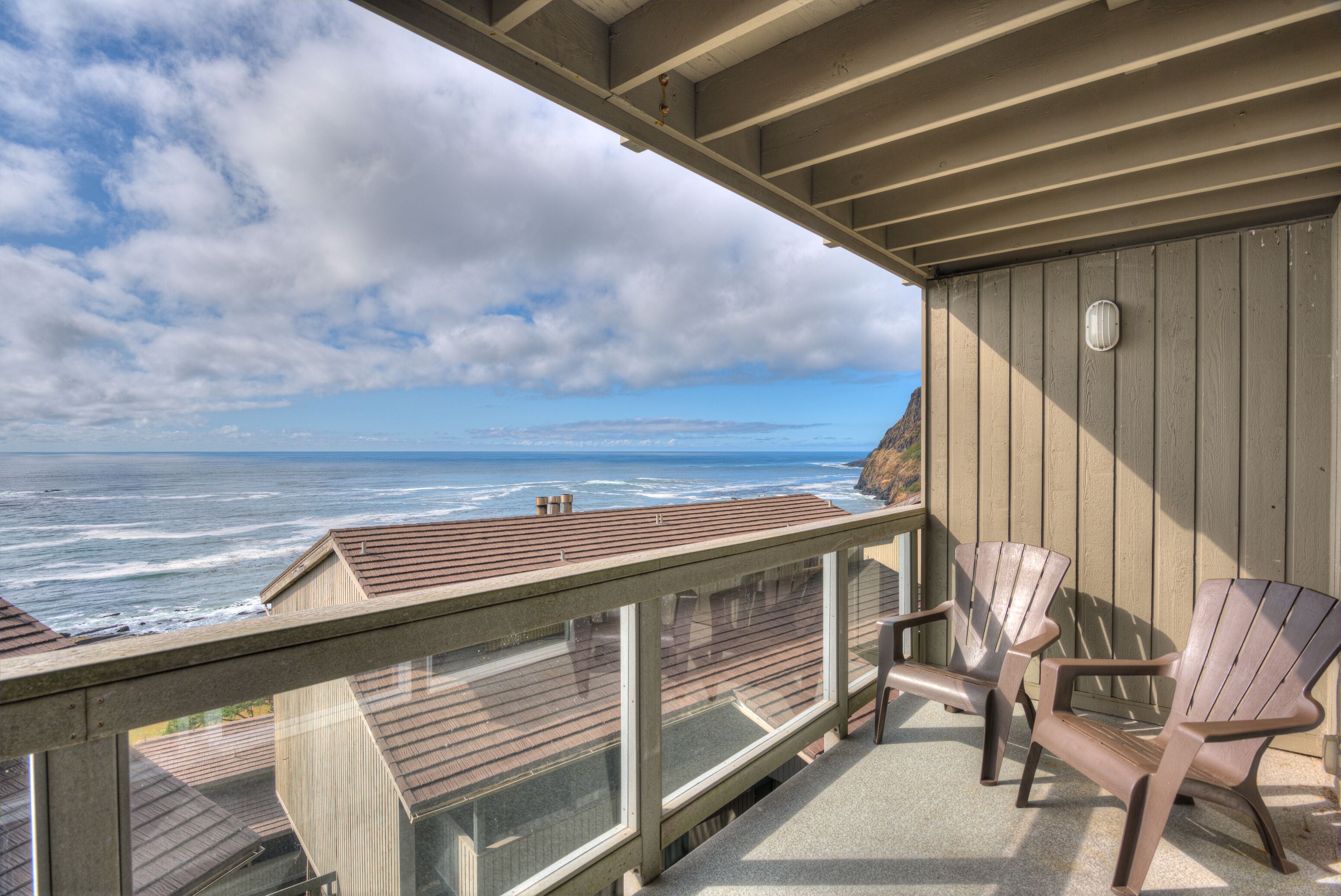 A balcony with a view of the ocean, wooden deck, and Adirondack chairs.
