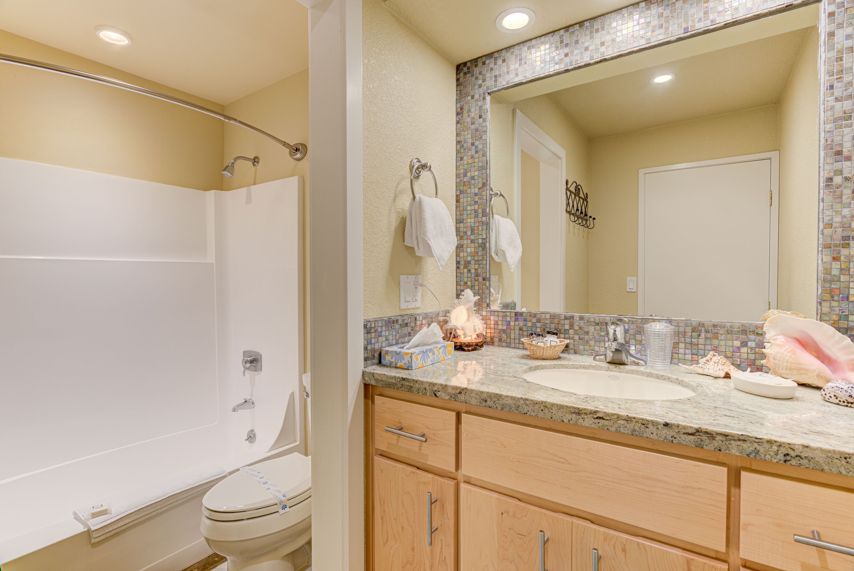A bathroom with a shower, toilet, vanity with a sink, and a large mirror.