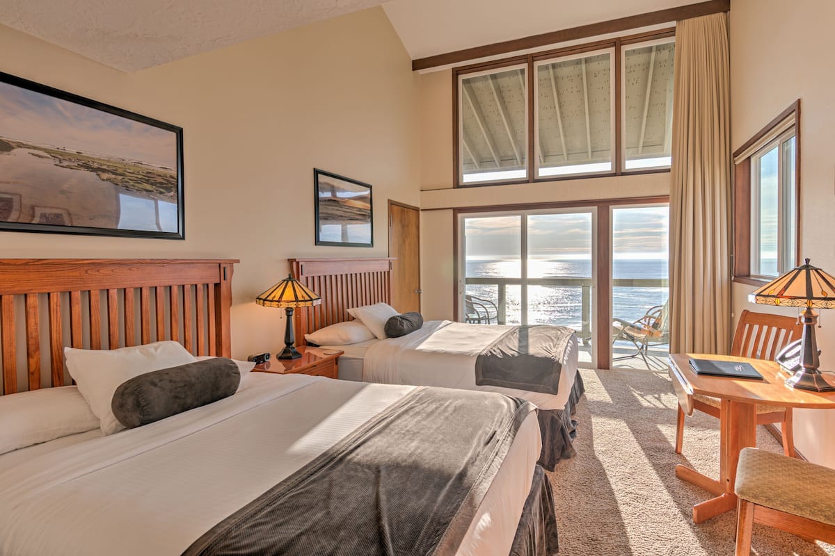 A hotel room with two beds, a desk, and a view of the ocean.