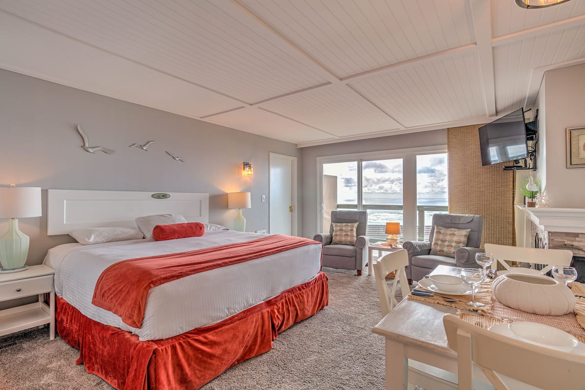 A hotel room with a large bed, two armchairs, a dining table set for two, and a TV mounted on the wall.