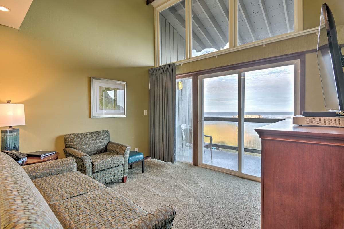 A spacious living room with a large window, a sofa, a chair, and a television on a wooden cabinet.