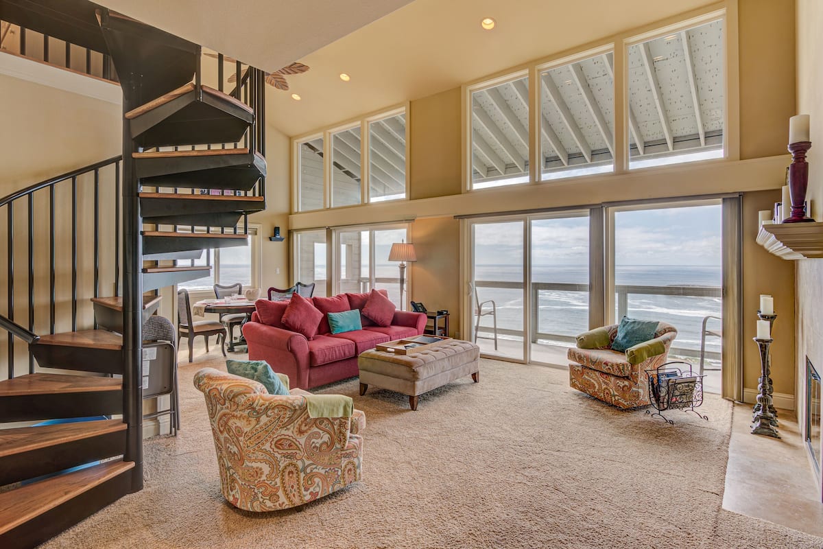 A spacious living area with a staircase, large windows, and a view of the ocean.