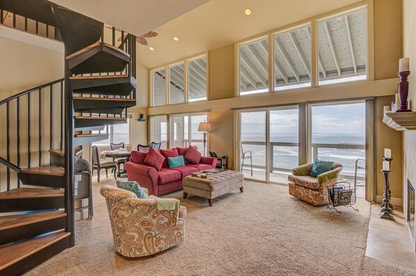 A spacious living area with a staircase, large windows, and a view of the ocean.