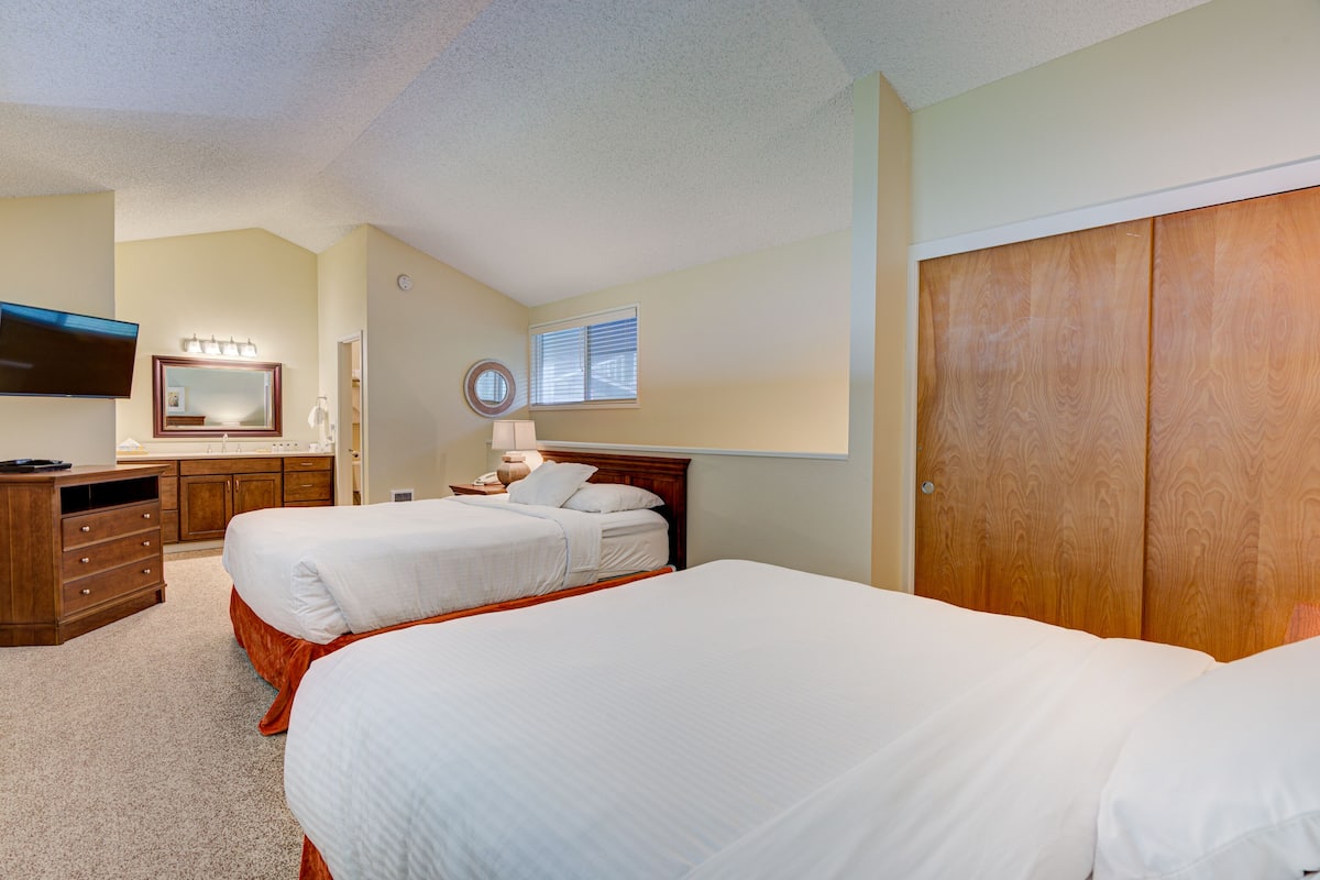 A hotel room with two beds, a wooden wardrobe, a vanity with a mirror, and a television.