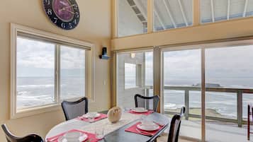 A dining area with a view of the ocean, a clock, and a table set for four.