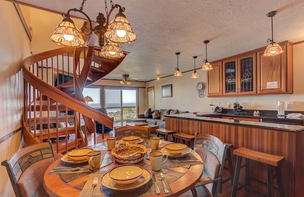 A dining area with a wooden table set for a meal, a spiral staircase, and wooden cabinets in the background.