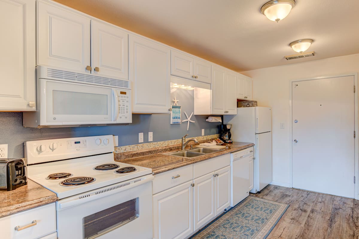 A kitchen with white cabinets, a microwave, stove, and a sink.