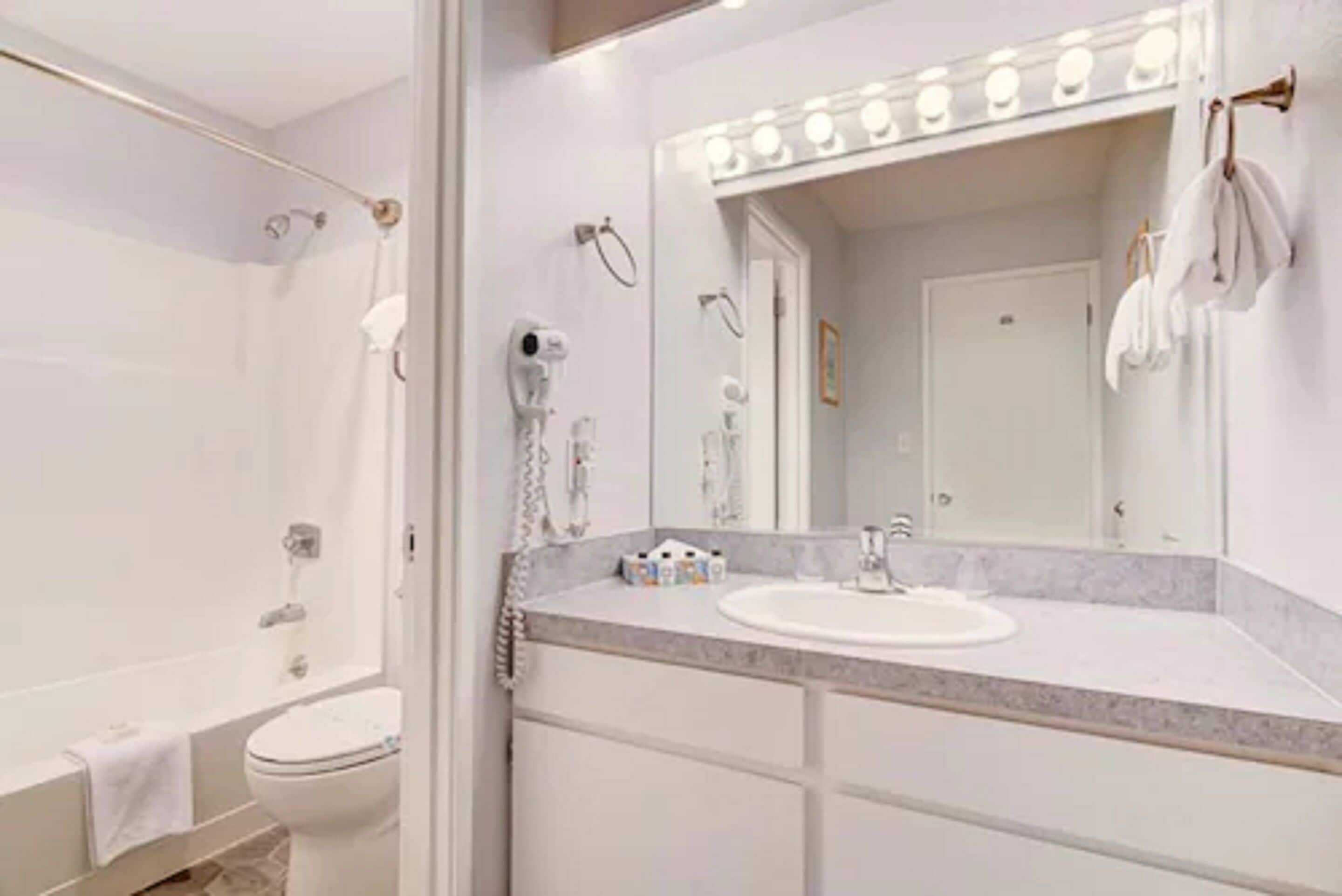 A modern bathroom with a white sink, vanity, and a large mirror with lights.