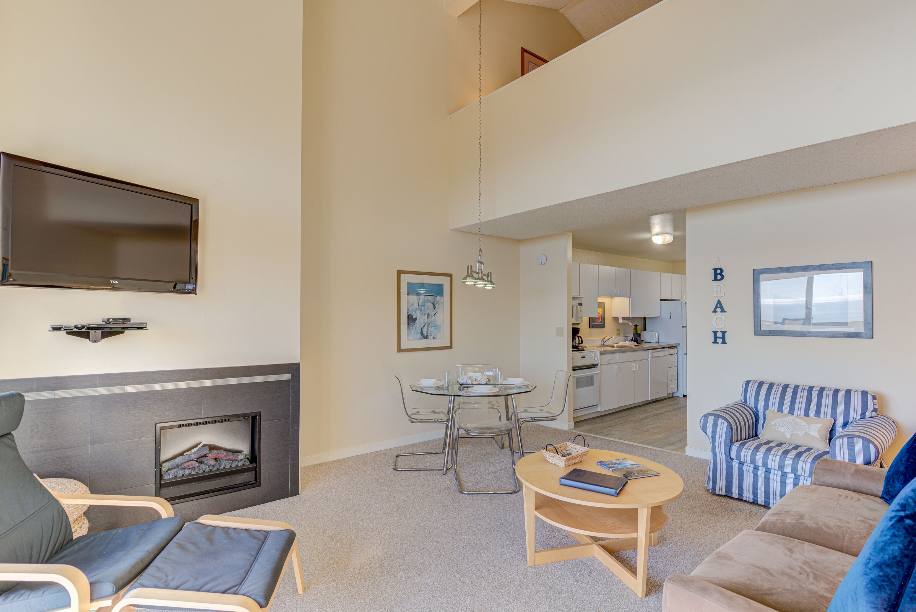 A modern living room with a fireplace, a dining area, and a kitchen in the background.