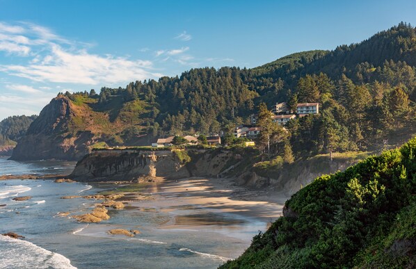 Un paisaje costero con una playa rocosa, un acantilado y un promontorio cubierto de bosque.