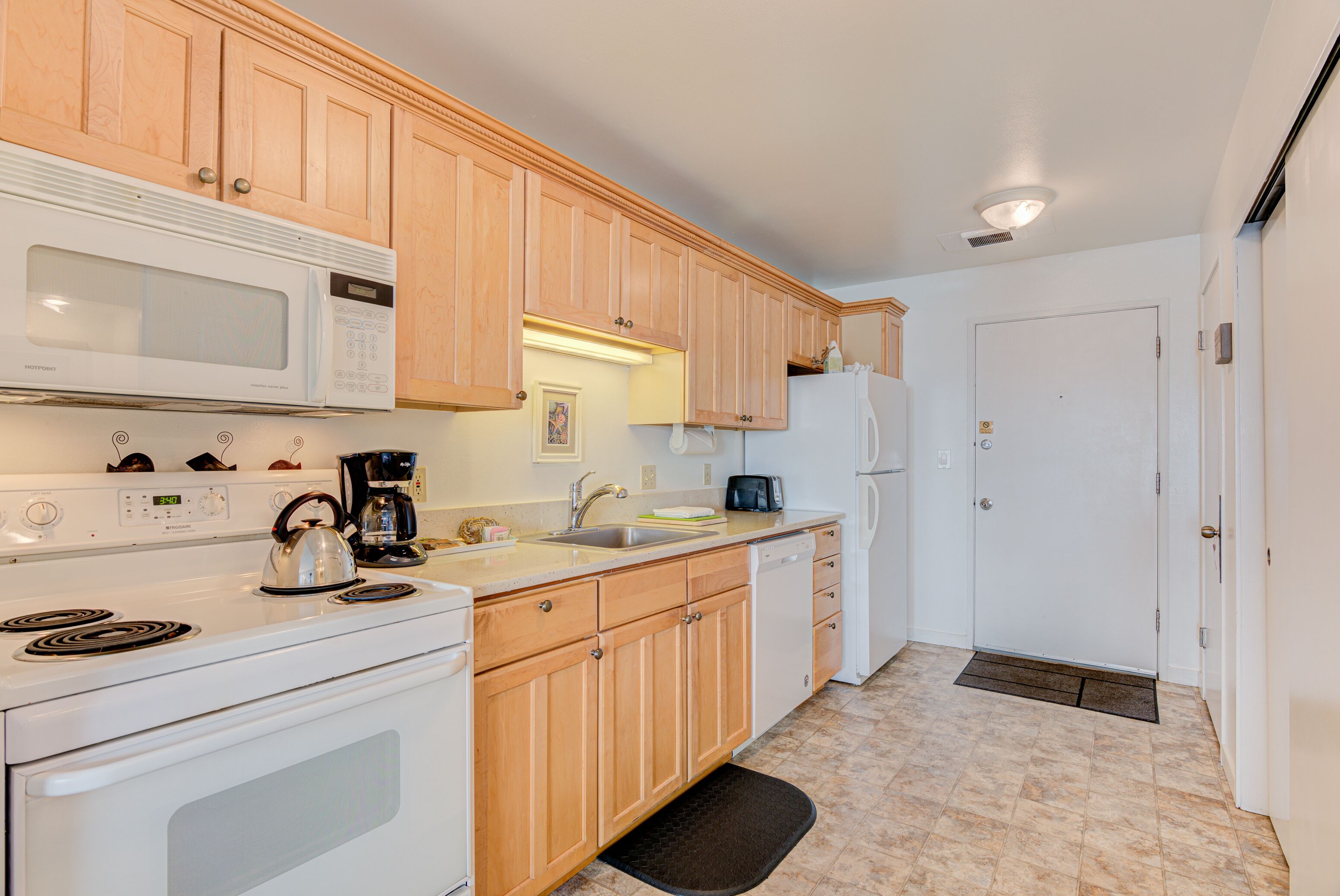 A kitchen with wooden cabinets, a white stove, a microwave, a coffee maker, and a refrigerator.