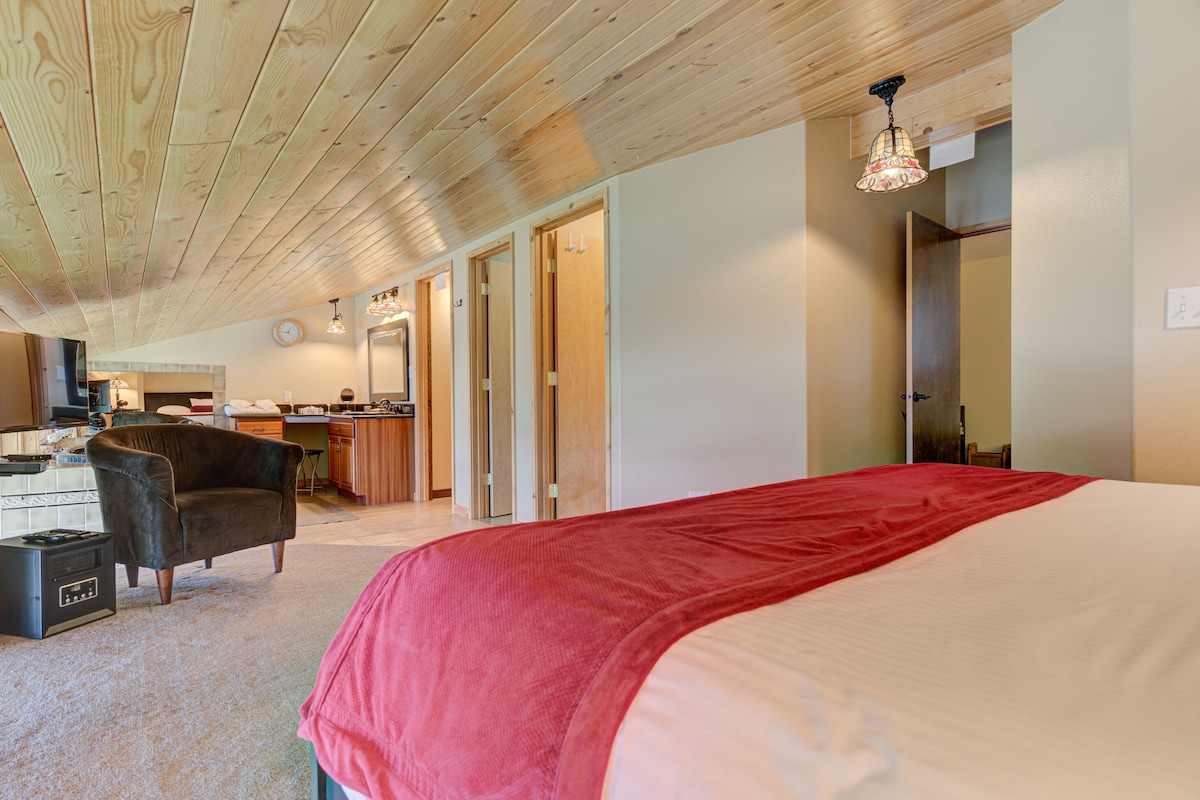 A bedroom with a large bed, a chair, a desk, and a kitchenette.