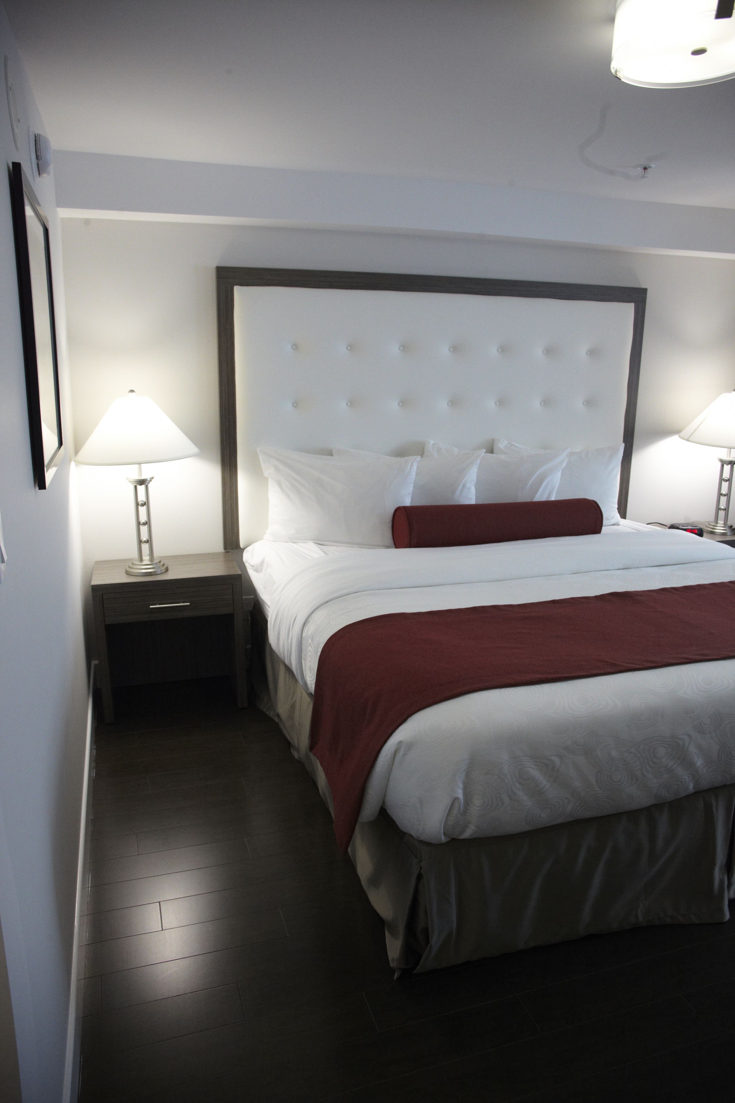 A neatly made bed with a white headboard and red accent pillows, flanked by two bedside tables with lamps.