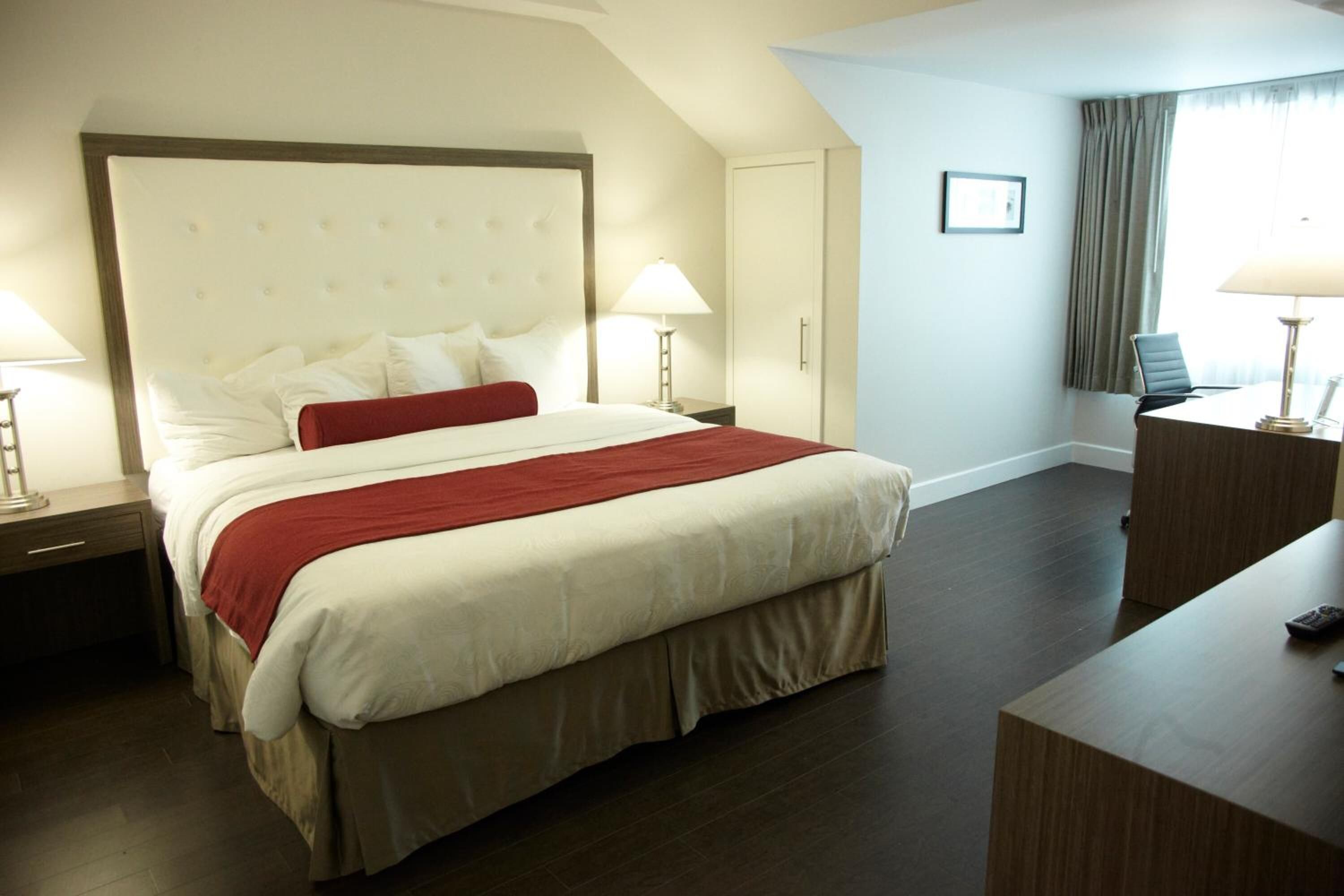 Quarto de hotel com uma cama grande, duas mesas de cabeceira, uma escrivaninha e uma cadeira.