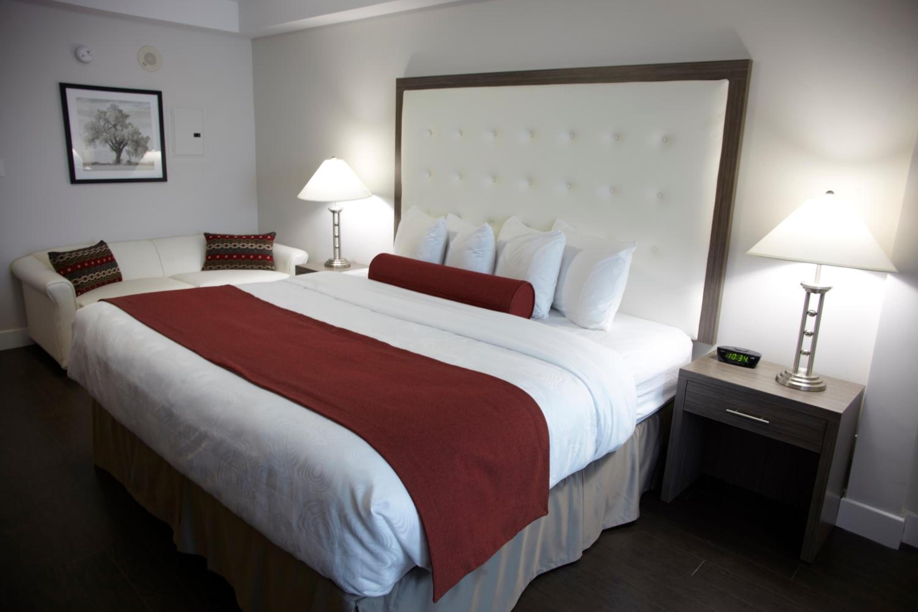 Habitación de hotel con una cama grande, una mesita de noche con lámpara, una mesita auxiliar y un cuadro en la pared.