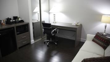 A hotel room with a desk, chair, and a white sofa.