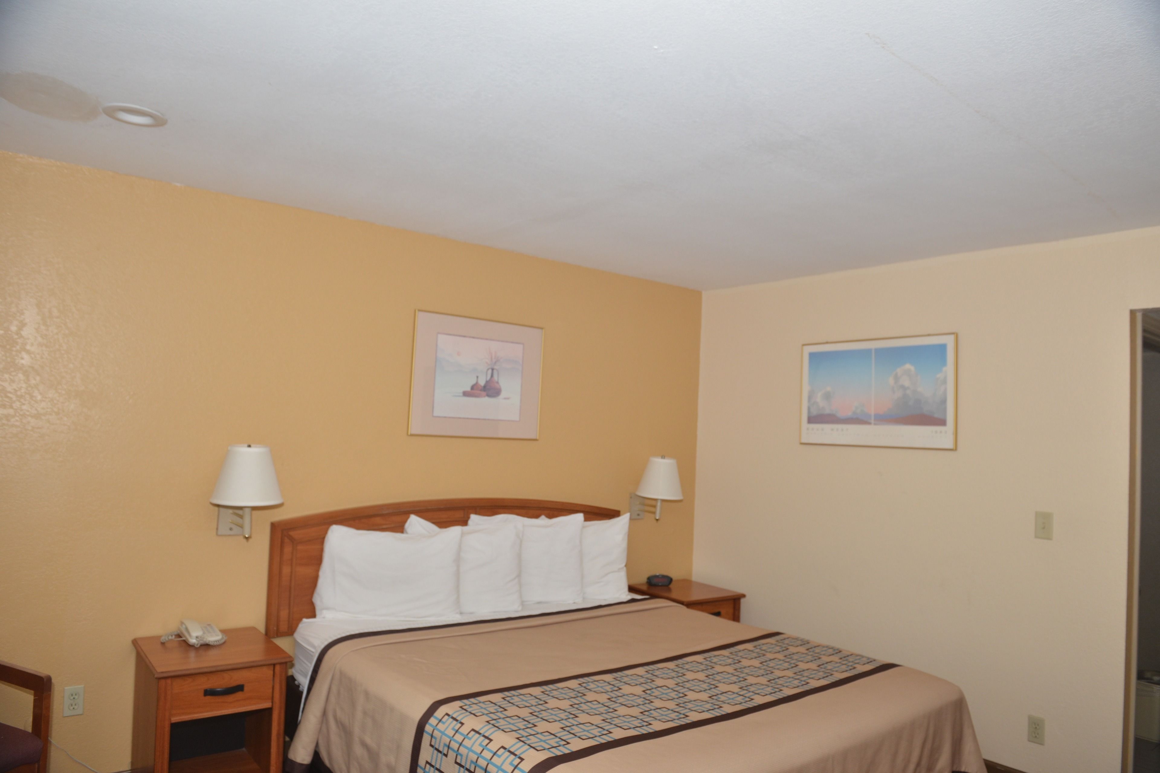 A hotel room with a bed, two bedside tables, a nightstand, and two wall-mounted lamps.