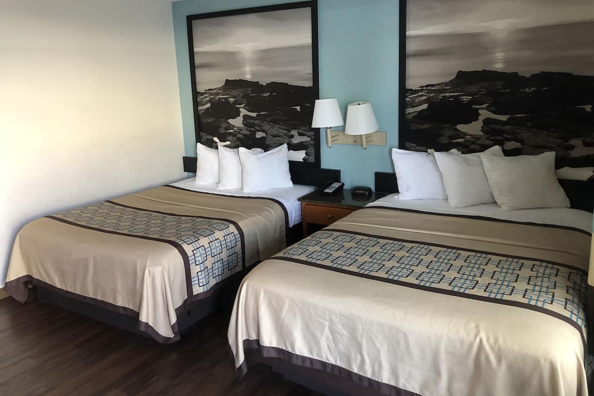 A hotel room with two beds, each with a patterned bedspread, a nightstand with a lamp, and a wall-mounted light fixture.